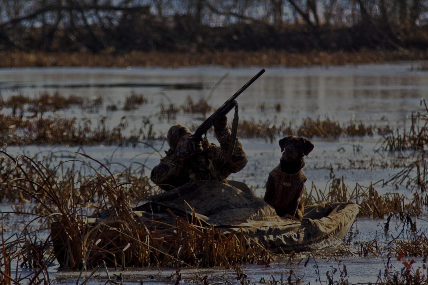 Two hunters and a dog set up in a marsh at dawn from a NuCanoe
