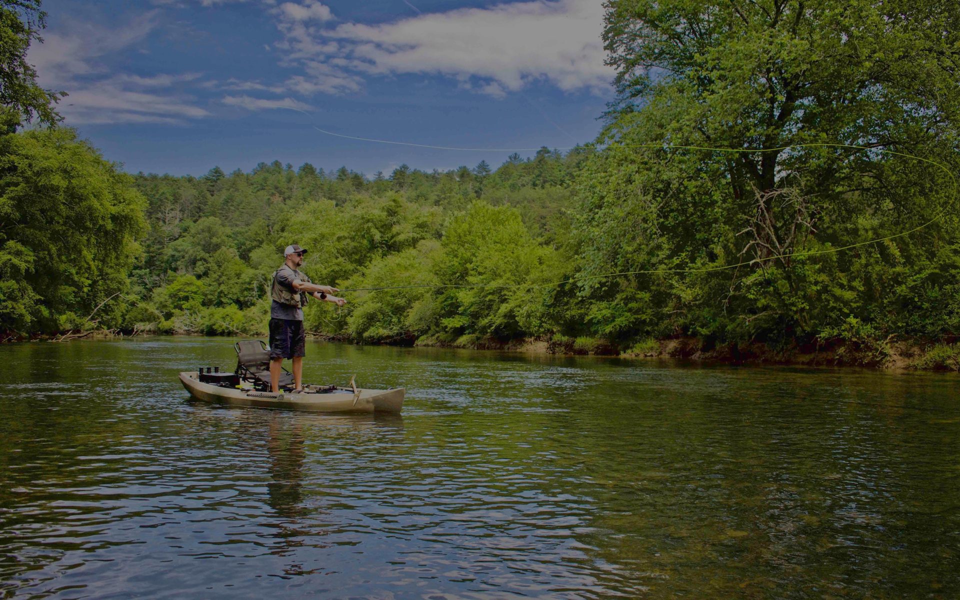 An angler standing and casting from a NuCanoe on a Vermont river